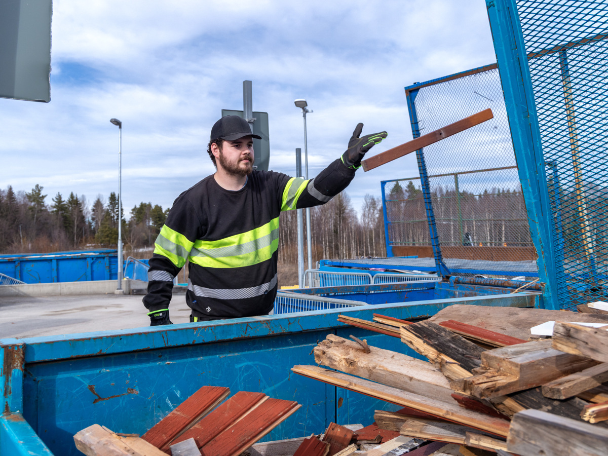 Medarbetare kastar trä i container på en återvinningscentral