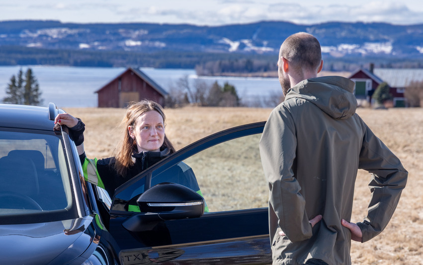 Två personer som står och pratar vid en bil