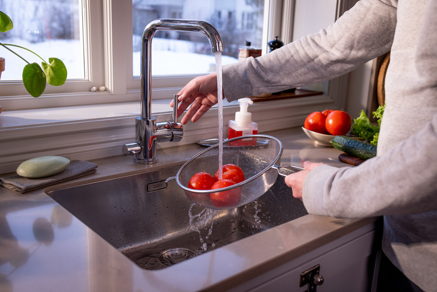 En person som sköjler tomater under kökskranen