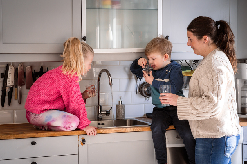Två barn med en kvinna håller i vattenglas, en av barnen dricker vatten